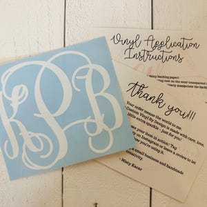 May include: A light blue vinyl decal with a white monogram of the letters R, S, and B. The decal is accompanied by two cards with handwritten text, including "Vinyl Application Instructions" and "thank you!!!".