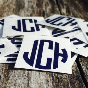 May include: A stack of white square stickers with a navy blue monogram of the letters JCH in a circle.