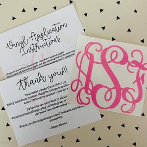 May include: A hot pink monogram vinyl decal with a cursive font, next to two white cards with black text. One card reads "Vinyl Application Instructions" and the other says "Thank you!!!". The background is a cream color with black triangles.