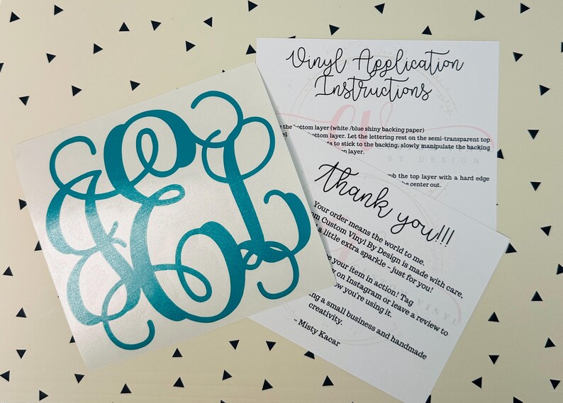 May include: A teal monogram vinyl decal with a cursive font, alongside instructions and a thank you note. The decal features the letters E, O, and L. The background is a cream color with black triangles.