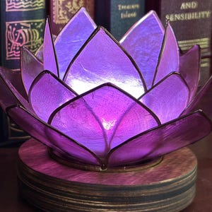 May include: A purple lotus-shaped LED light display on a circular wooden base. Text reads: Blossom Programmable LED Light Display, Wi-Fi Enabled, No Apps Required, Create Animations, Play Meditations, Control from Any Device, Be. Breathe. Blossom.