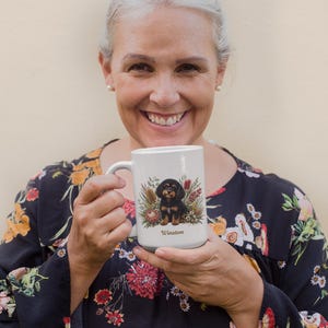 May include: A white ceramic mug featuring a colorful illustration of a black and tan puppy surrounded by various flowers and foliage. The name Winston is printed in brown script below the puppy. The mug has a handle on the left side.
