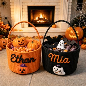 Peut inclure: Deux paniers ronds en corde pour Halloween, un orange et un noir. Le panier orange porte le nom Ethan et une citrouille, tandis que le panier noir porte le nom Mia et un fantôme. Les deux sont remplis de petites citrouilles et de bonbons.