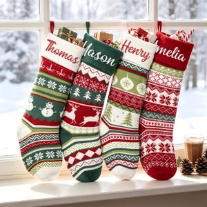 Può includere: Quattro calze natalizie in maglia appese in fila, ognuna con un risvolto bianco personalizzato con i nomi Thomas, Mason, Henry e Amelia. Le calze presentano motivi festivi tra cui pupazzi di neve, renne, alberi e fiocchi di neve.