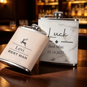 May include: Two stainless steel flasks with screw-top caps. One flask is wrapped in light tan material featuring a deer silhouette, the name Levi, and the text BEST MAN. The other is white with a marble pattern, the word Luck, Best Man, and 02.14.2027.