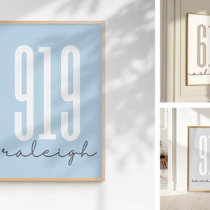 May include: A vertical rectangular wall art print in a light wood frame featuring the number 919 in large white sans-serif font and the word raleigh in a dark grey cursive script on a light blue background, with two additional variations shown.
