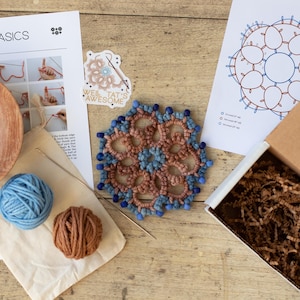 May include: A tatting craft kit featuring a circular brown and blue lace doily with beads, a wooden bowl with blue beads, two balls of yarn, a printed instruction sheet titled TATTING BASICS, a pattern diagram, a sticker, and a cardboard box.