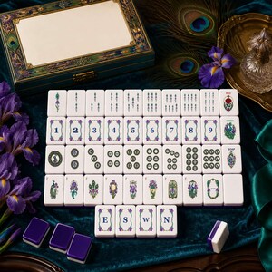 May include: A set of white mahjong tiles featuring intricate floral and peacock illustrations, numbers one through nine, and directional letters E, S, W, and N. The tiles are arranged in a grid alongside a decorative storage box with peacock motifs.