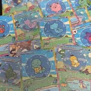 May include: A collection of holographic trading cards featuring various Pokémon characters like Squirtle, Mew, Mewtwo, and Psyduck. Each card displays a central circular illustration of a character, text detailing abilities and attacks, and a sparkling blue background.