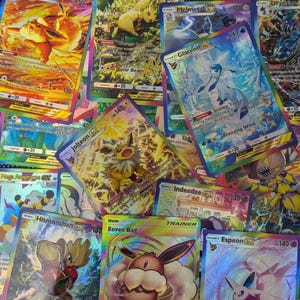 May include: A collection of colorful trading cards featuring various creatures and characters with holographic finishes. Visible names include Glaceon ex, Jolteon ex, Melmetal ex, Hitmonchan ex, Espeon ex, Indeedee ex, and an Eevee Bag trainer card.
