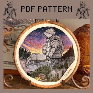 May include: A circular embroidery hoop containing a hand-stitched depiction of a large grey robot sitting in a forest landscape at sunset. The sky features purple and orange gradients, and the robot has a single glowing yellow eye. Text reads PDF PATTERN.