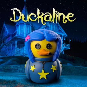 Op de afbeelding: Een gele rubberen eendfiguur met blauw haar, zwarte knoopogen en een oranje snavel. De eend draagt een donkerblauwe outfit versierd met gele sterren en een kleine sleutelhanger. Het woord Duckaline staat in het geel boven de figuur afgebeeld.