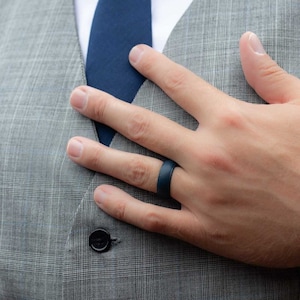May include: A hand wearing a dark blue silicone ring. The hand is resting on a gray plaid fabric.