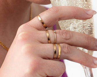 Puede incluir: Una persona con anillos de oro en los dedos sostiene una copa de champán llena de vino espumoso.