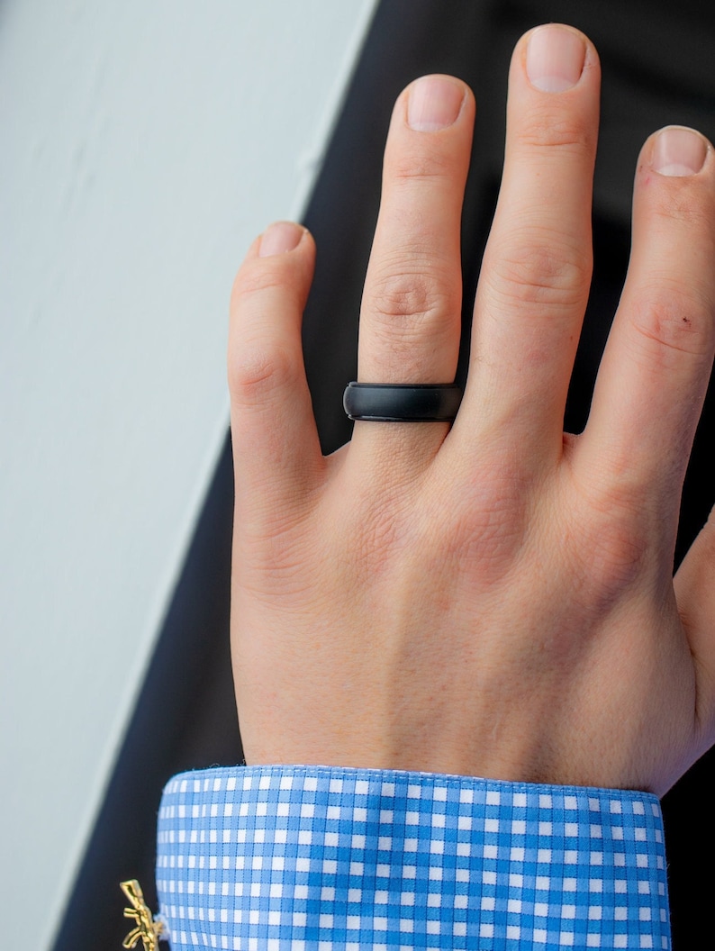 Op de afbeelding: Een zwarte siliconen ring aan een vinger. De ring is simpel en modern ontworpen.