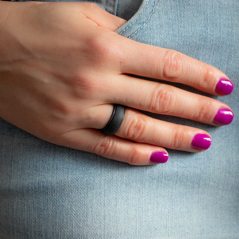 Op de afbeelding: Een zwarte siliconen ring gedragen op een vinger met roze nagellak.
