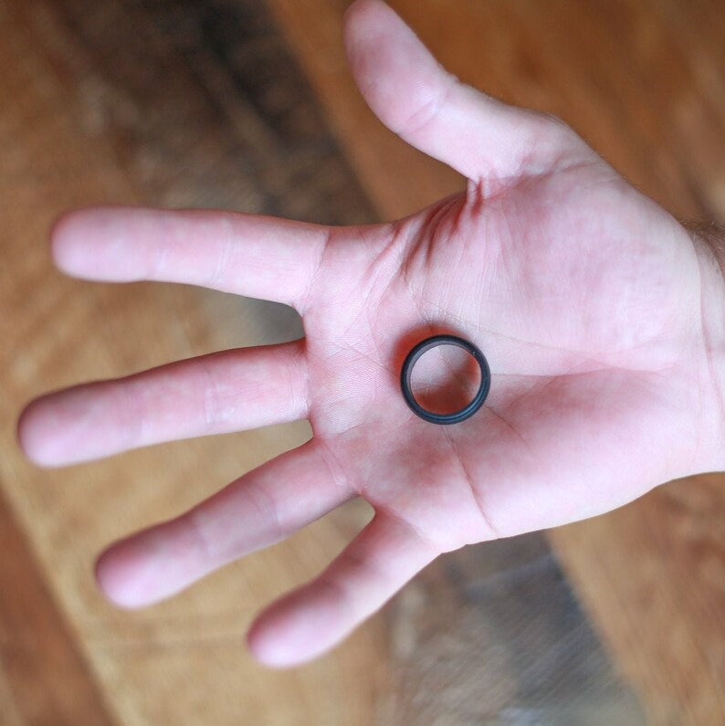 Op de afbeelding: Een zwarte siliconen ring op een open hand.