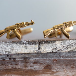 May include: A pair of gold-toned cufflinks shaped like assault rifles.