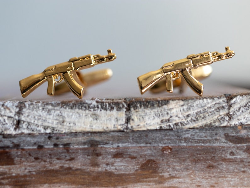 May include: A pair of gold-toned cufflinks shaped like assault rifles.