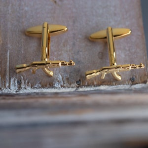 May include: A pair of gold cufflinks featuring a detailed miniature rifle design.