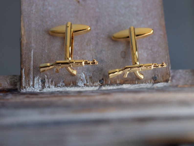 May include: A pair of gold cufflinks featuring a detailed miniature rifle design.