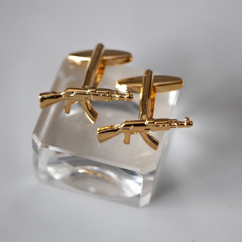 May include: A pair of gold-tone cufflinks featuring a detailed design of an AK-47 assault rifle.