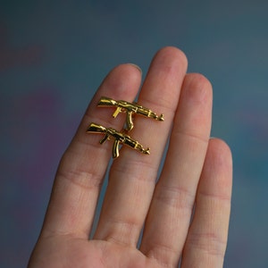 May include: A pair of gold-coloured earrings shaped like AK-47 rifles.