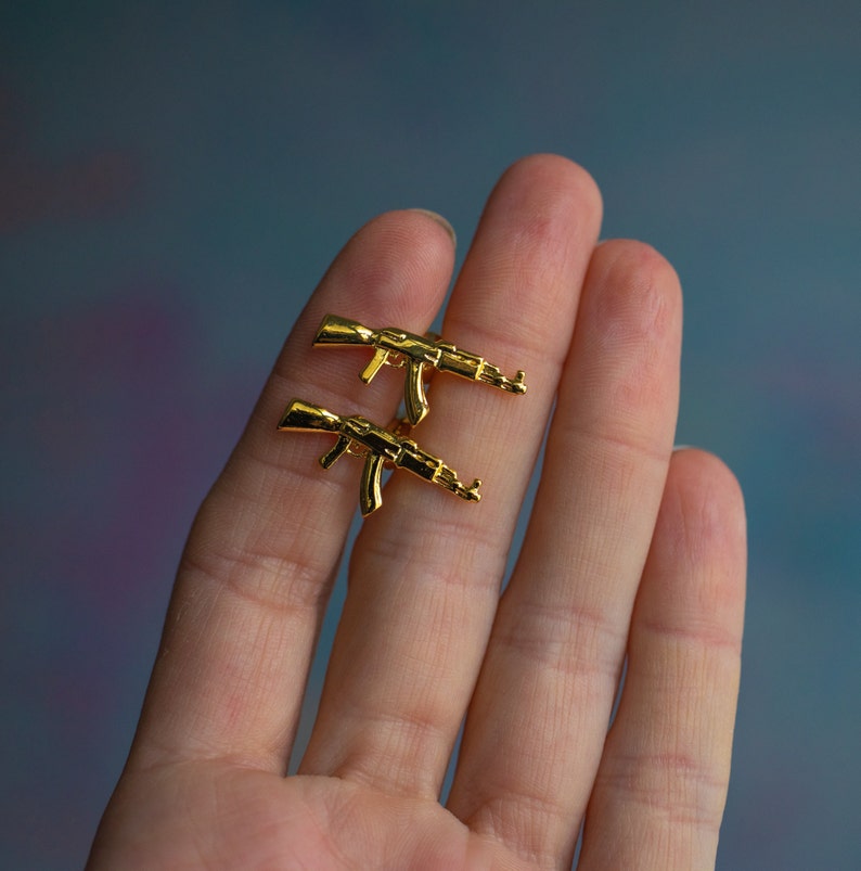 May include: A pair of gold-coloured earrings shaped like AK-47 rifles.