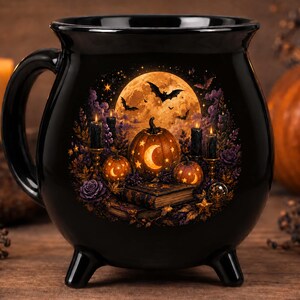 May include: A black ceramic cauldron-shaped mug featuring a detailed graphic of a glowing full moon, flying bats, carved pumpkins with crescent moon cutouts, lit black candles, and old books surrounded by purple flowers and autumn foliage.