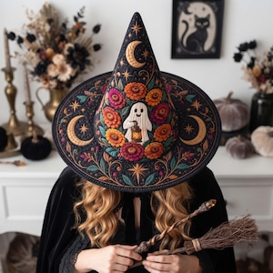 May include: A black pointed hat featuring embroidered orange and pink flowers, gold crescent moons, stars, and a central white ghost figure holding a lantern. The hat has a wide brim and intricate stitching throughout the fabric design.
