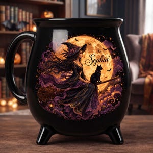 Peut inclure: Un mug noir en forme de chaudron orné d'une illustration représentant une sorcière en robe violette et noire sur un balai avec un chat noir devant une grande pleine lune jaune. Le prénom Sophia est inscrit en lettres cursives noires sur la lune.
