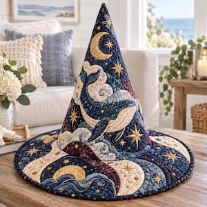 May include: A quilted cone-shaped hat featuring a dark blue background with a large whale, a crescent moon, and golden stars. The fabric displays intricate stitching patterns, swirling clouds, and ocean waves in shades of blue, cream, and gold.