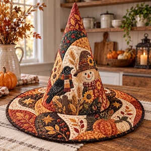 May include: A quilted fabric witch hat featuring a fall-themed design with a scarecrow, a black crow, sunflowers, wheat stalks, and pumpkins. The hat is decorated with a patchwork pattern of autumn leaves in shades of orange, brown, and gold.