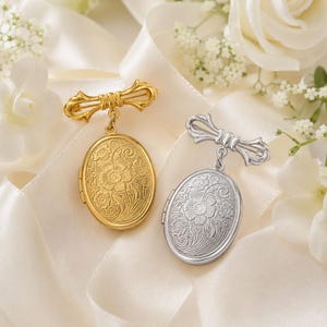 Pode incluir: Dois relicários ovais, um em tom dourado e outro em tom prateado, cada um com uma gravação floral intrincada na frente. Ambos os relicários estão suspensos por um broche de metal em forma de laço a condizer com uma dobradiça lateral.