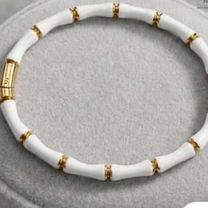 May include: A circular bracelet featuring alternating segments of smooth white material and polished gold-tone metal. The design mimics the appearance of bamboo stalks, connected by gold-tone rings. A gold-tone clasp mechanism is integrated into the band.