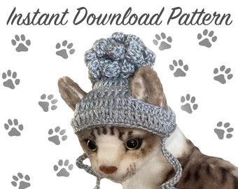 May include: A gray crocheted cat hat with a pom-pom on top. The hat has long ties that hang down the sides. The hat is on a cat's head.