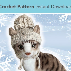 May include: A crocheted cat hat with a white pom pom. The hat is beige with brown flecks and has a long tie. The hat is on a stuffed cat.