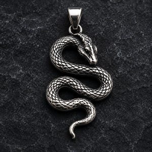 Puede incluir: Un colgante de metal plateado con forma de serpiente enroscada con texturas de escamas detalladas en todo el cuerpo. La serpiente está colocada en forma de S con la cabeza hacia la derecha, con un acabado pulido y una anilla en la parte superior.