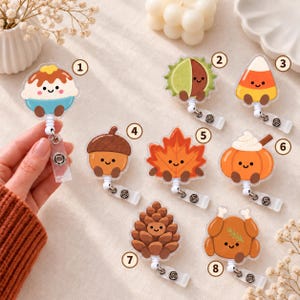 May include: A collection of eight acrylic badge reels featuring cute, smiling characters: a dessert, chestnut, candy corn, acorn, maple leaf, pumpkin, pinecone, and roasted turkey. Each item is numbered one through eight with a metal clip.