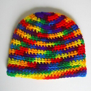 May include: A colorful crocheted beanie hat with a rainbow pattern. The hat is made with a variety of colors, including red, orange, yellow, green, blue, indigo, and violet.