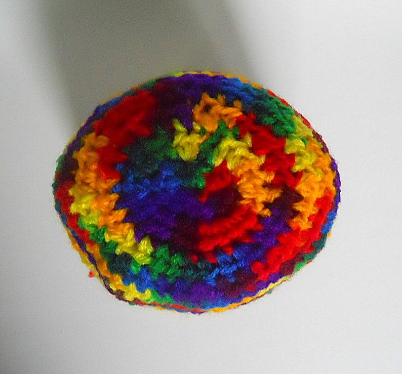 May include: A colorful crocheted hat with a rainbow pattern. The hat is made of yarn in shades of red, orange, yellow, green, blue, indigo, and violet.