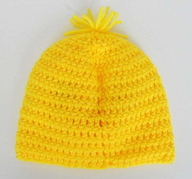 May include: A bright yellow crocheted beanie with a fluffy pom-pom on top.