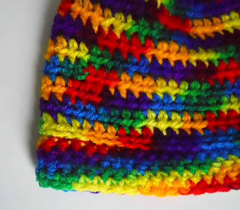 May include: A colorful crocheted hat with stripes of red, orange, yellow, green, blue, indigo, and violet.