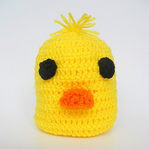 May include: A yellow crocheted hat shaped like a chick with black eyes and an orange beak.