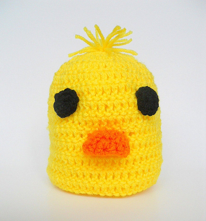 May include: A yellow crocheted hat shaped like a chick with black eyes and an orange beak.