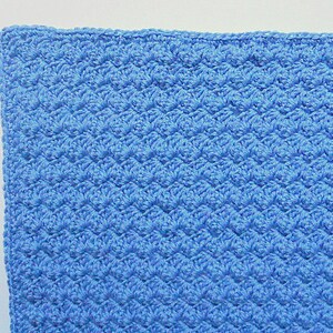 May include: A close-up of a blue crocheted blanket with a textured pattern.