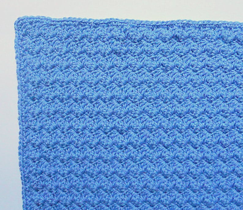 May include: A close-up of a blue crocheted blanket with a textured pattern.