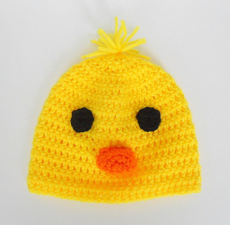 May include: A yellow crocheted baby hat with black eyes, an orange nose, and a yellow pom-pom on top.