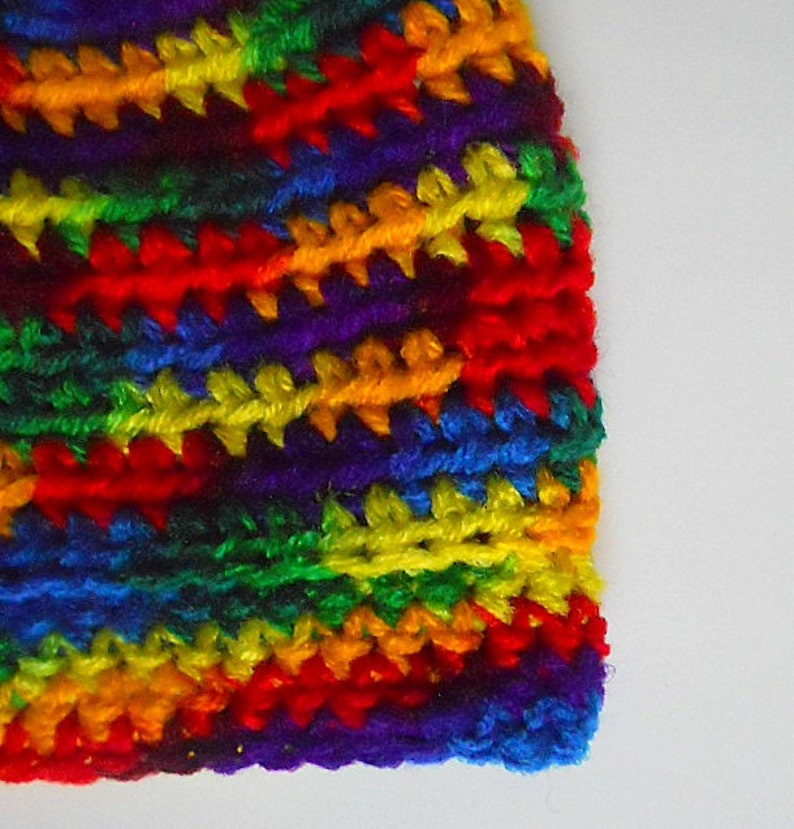 May include: A colorful crocheted hat with a rainbow pattern. The hat is made with different shades of red, orange, yellow, green, blue, and purple yarn.
