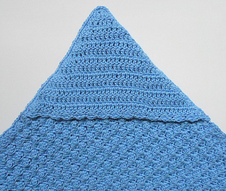May include: A light blue crocheted baby blanket with a pointed hood. The blanket is made with a textured stitch and has a scalloped edge.
